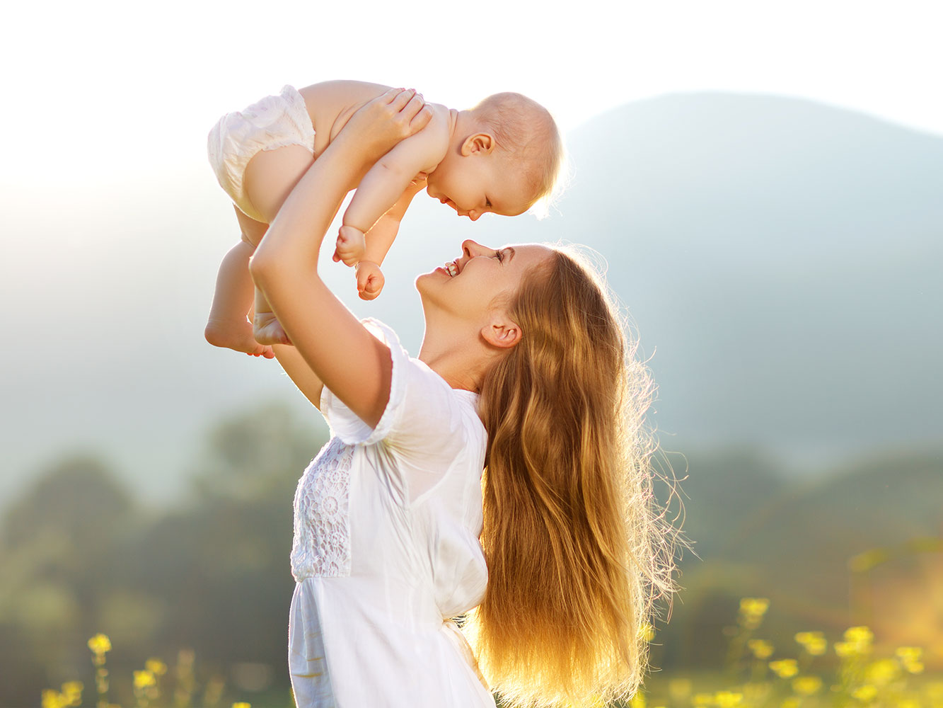 New Mom Standing in Field Holding Newborn Baby in Air - KeepsakeMom