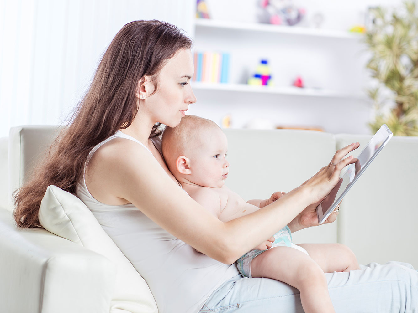 Mother Customizing Breast Milk Jewelry Design On Tablet - Sitting on Couch with Baby in Lap - KeepsakeMom