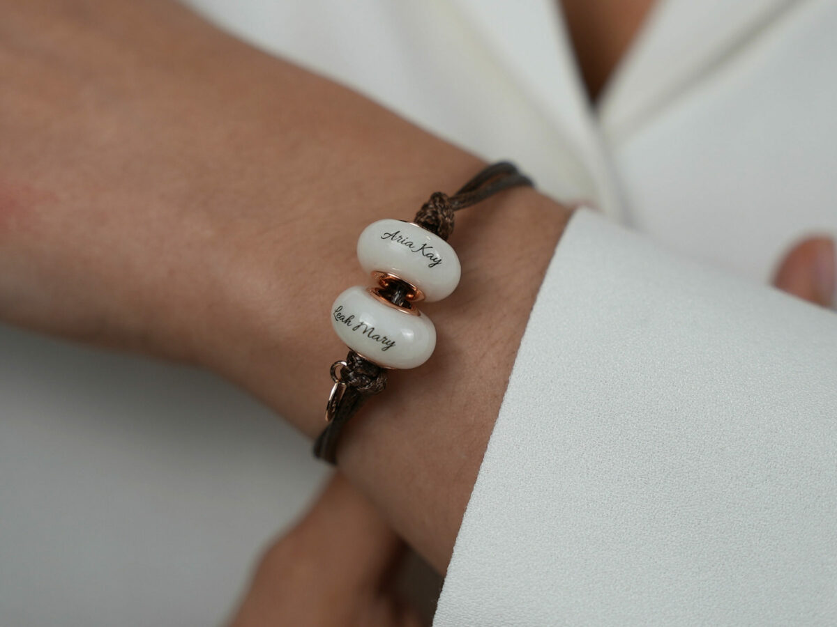2 breastmilk jewelry beads brown cord bracelet with rose gold bead cores and tag with child's name on the bead engraved from KeepsakeMom on a model wrist