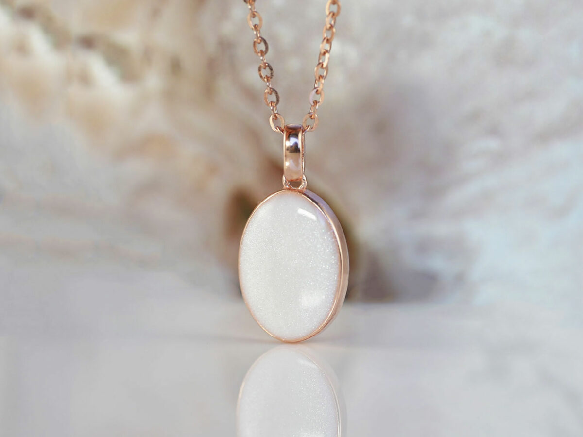 breastmilk jewelry oval simple necklace from keepsakemom in rose gold setting on light background with pearl powder in milk stone