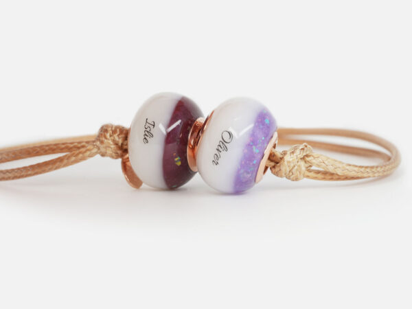 breastmilk two beads bracelet with birth month colors garnet and alexandrite and names on the breastmilk part of the beads on a waxed light brown cord on white background from KeepsakeMom