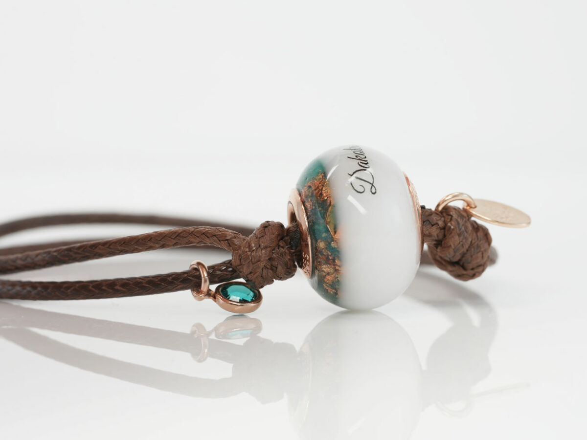breastmilk one bead bracelet with birth month colors of turquoise, and name on the breastmilk part of the bead on a waxed brown cord on white background from KeepsakeMom