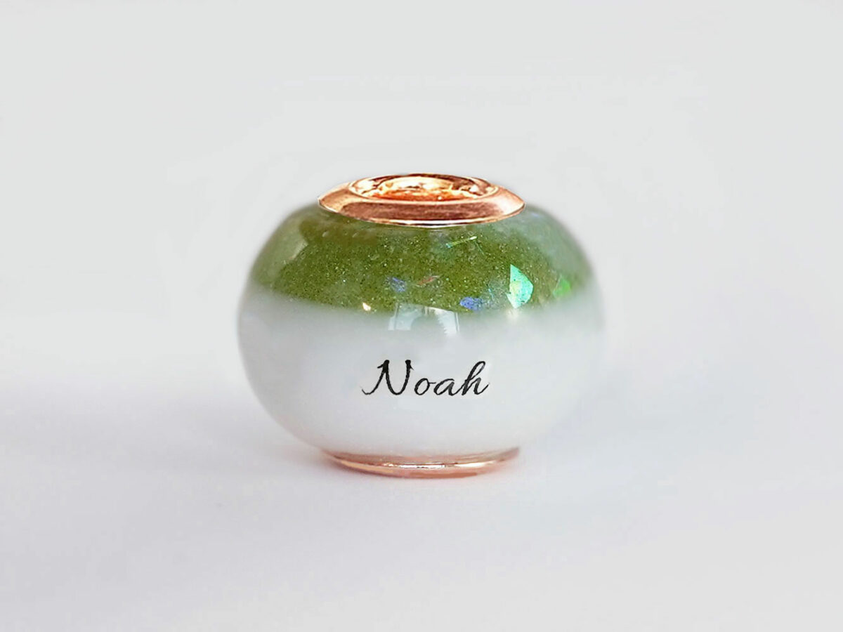 breastmilk bead with birth month color august peridot green with opal flakes at the top and child's name in the milk engraved with rose gold cores from KeepsakeMom on white background