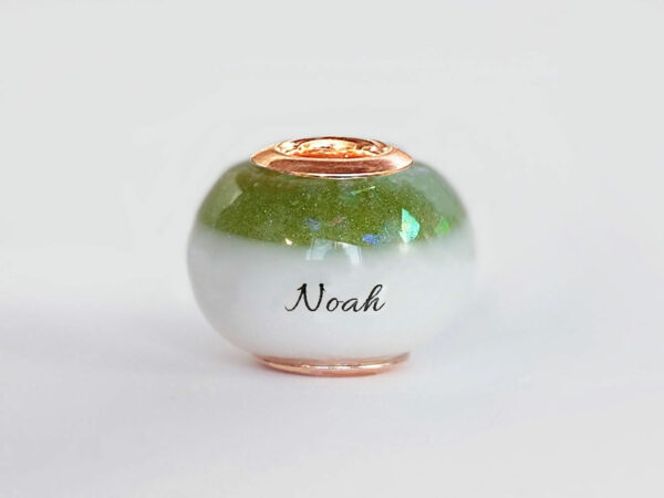 breastmilk bead with birth month color august peridot green with opal flakes at the top and child's name in the milk engraved with rose gold cores from KeepsakeMom on white background
