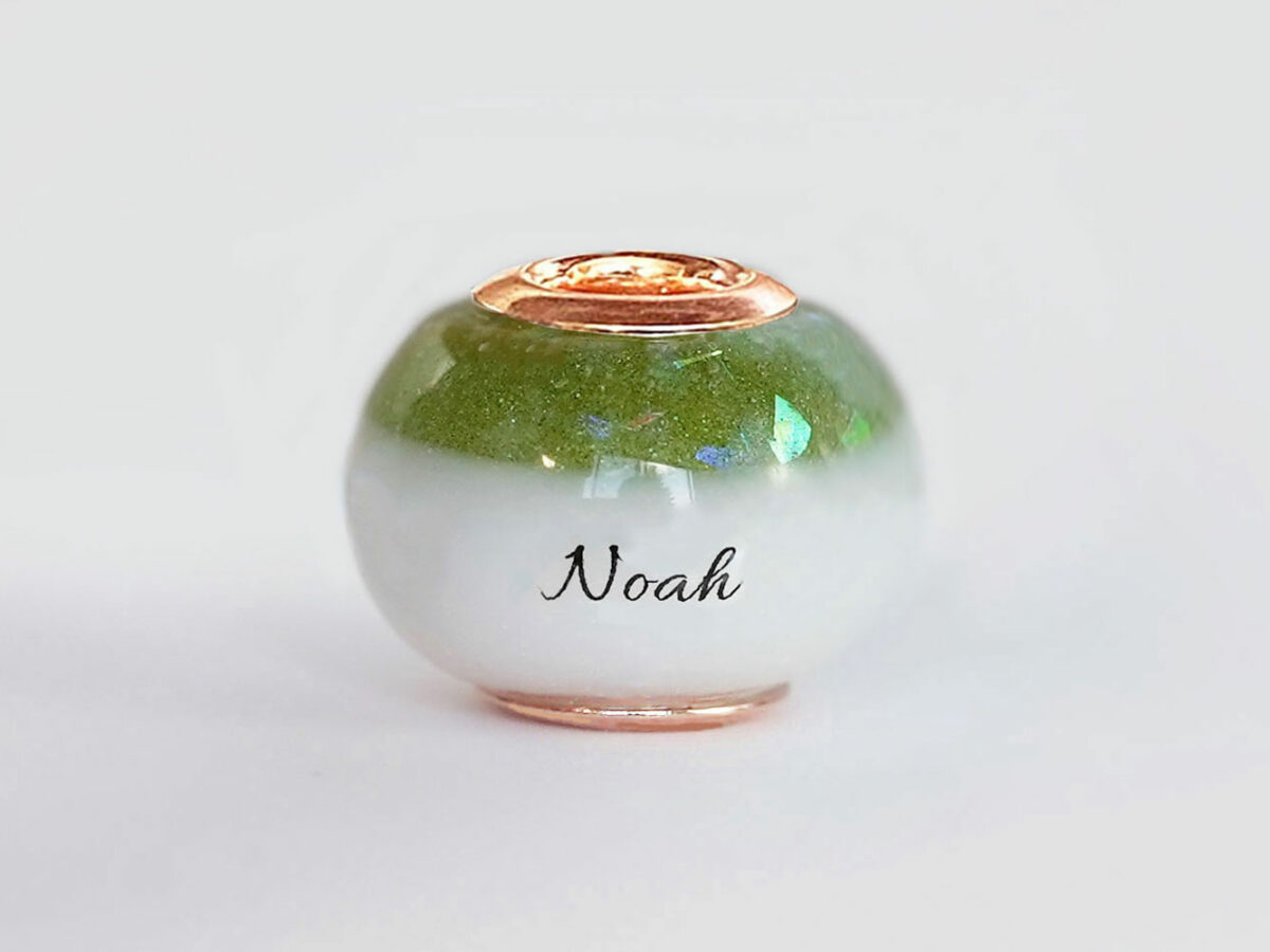 breastmilk bead with birth month color august peridot green with opal flakes at the top and child's name in the milk engraved with rose gold cores from KeepsakeMom on white background