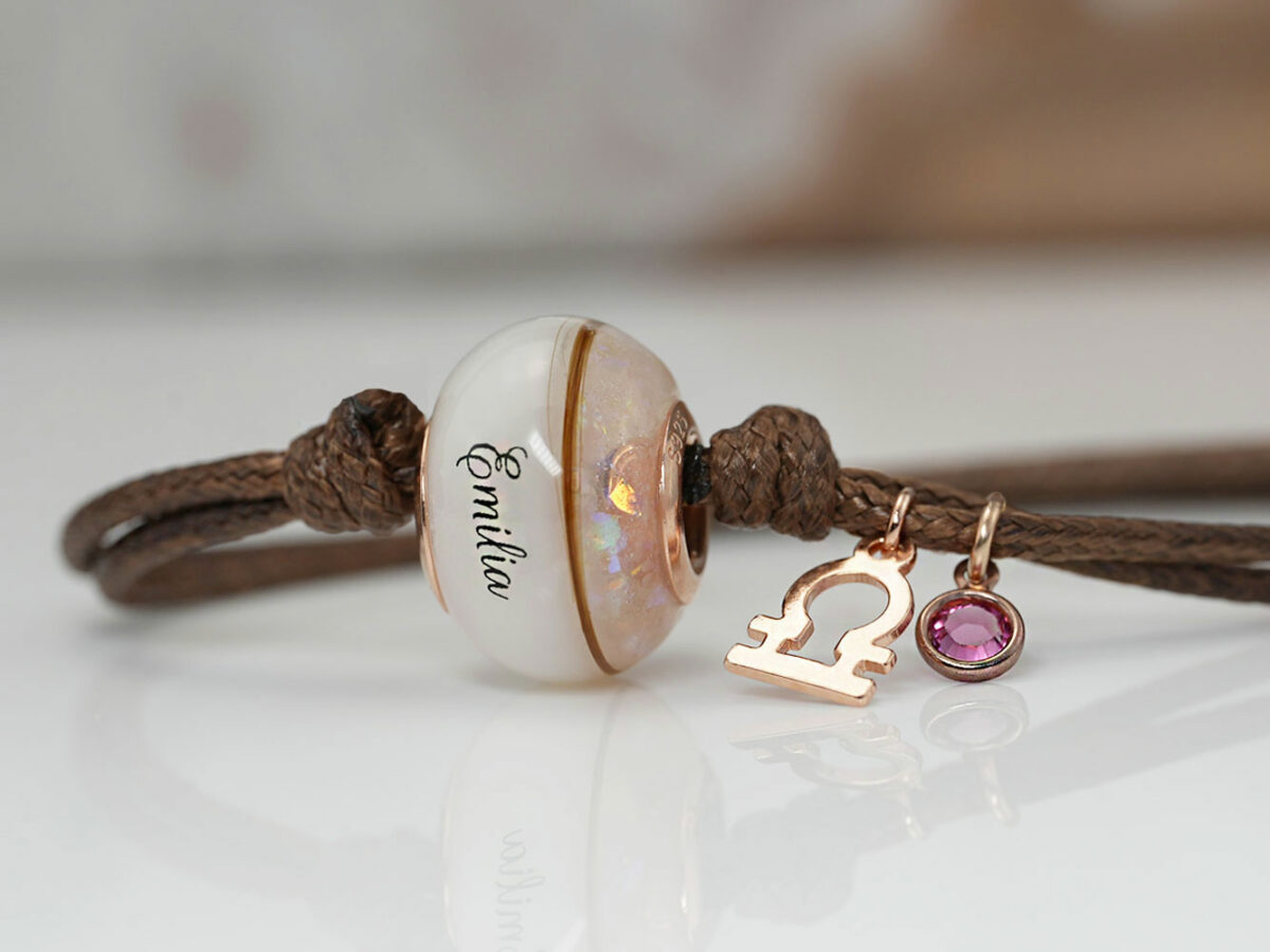breastmilk one bead bracelet with birth month colors of pink with opal flakes, hair and name on the breastmilk part of the bead on a waxed brown cord on white background from KeepsakeMom with charms