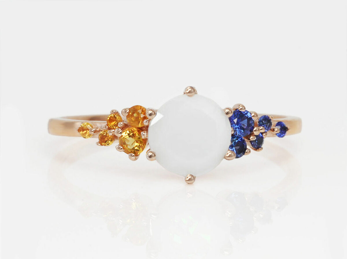 breast milk ring on a white background in rose gold and november citrine crystals on one side and dark blue crystals on the other side of a central diamond-shaped breast milk stone from keepsakemom