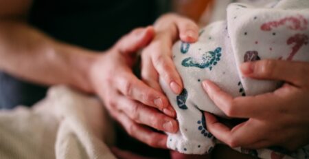 Closeup hands of mom and dad holding newborn baby