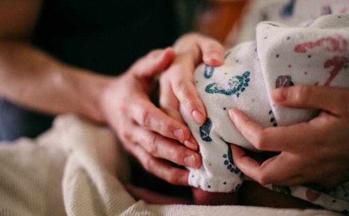 Closeup hands of mom and dad holding newborn baby