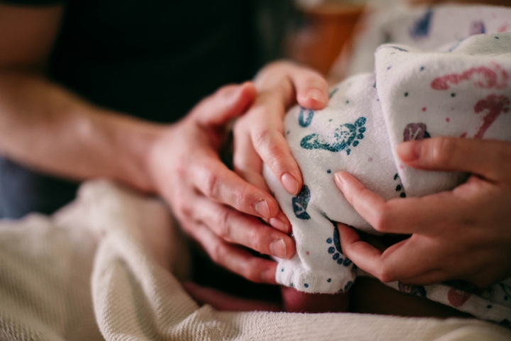 Closeup hands of mom and dad holding newborn baby