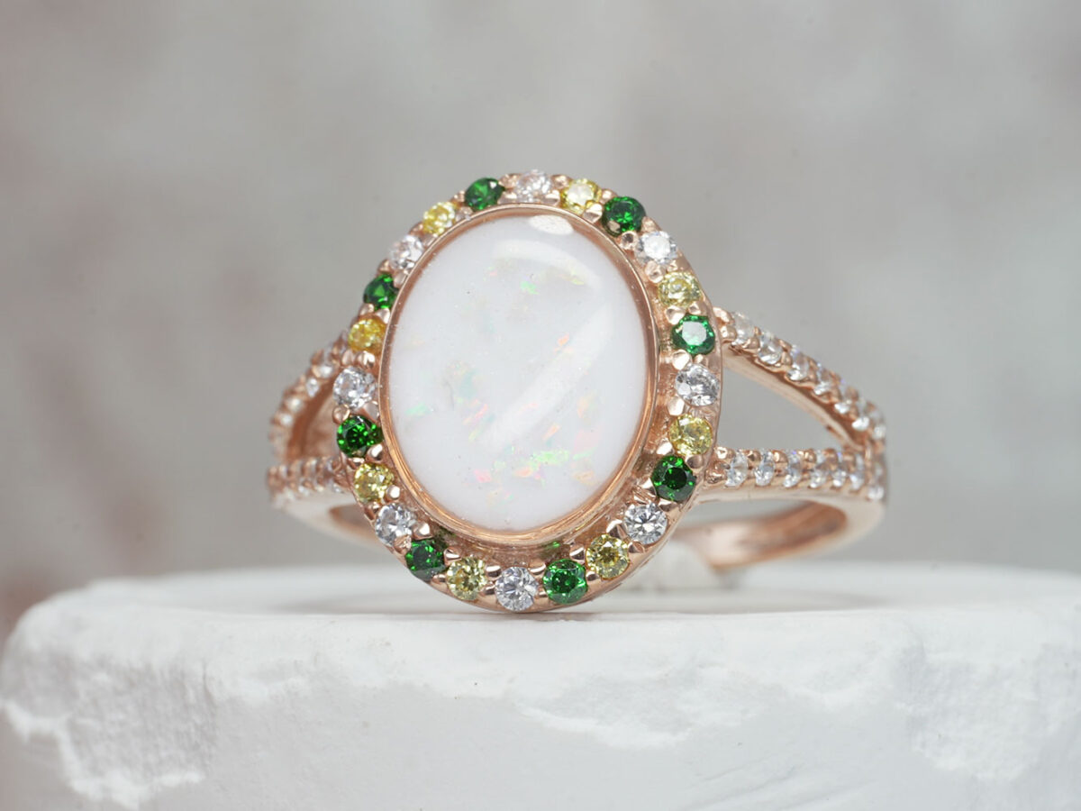 breastmilk ring with oval shaped central breastmilk stone with alternating green, yellow and clear crystals or gems as halo around the stone and around the ring band from keepsakemom in rose gold setting