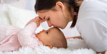 Portrait of a mother kissing her baby daughter on the bed - KeepsakeMom