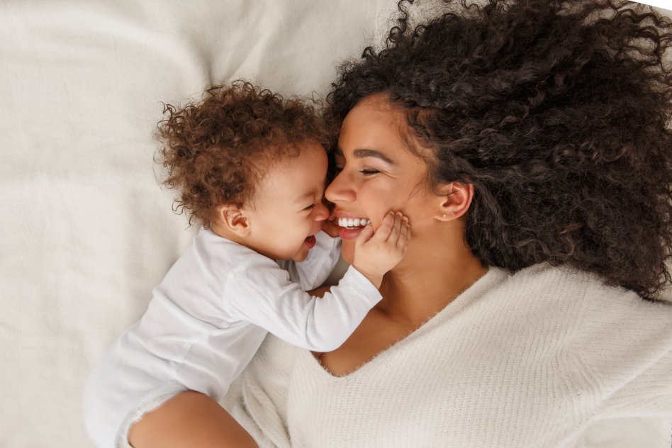 Happy mom and baby on the bed smiling and laughing