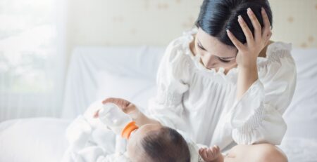 Tired mother feeding baby with a bottle in bed