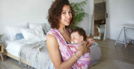 Young mother holding her child in a baby wearing carrier