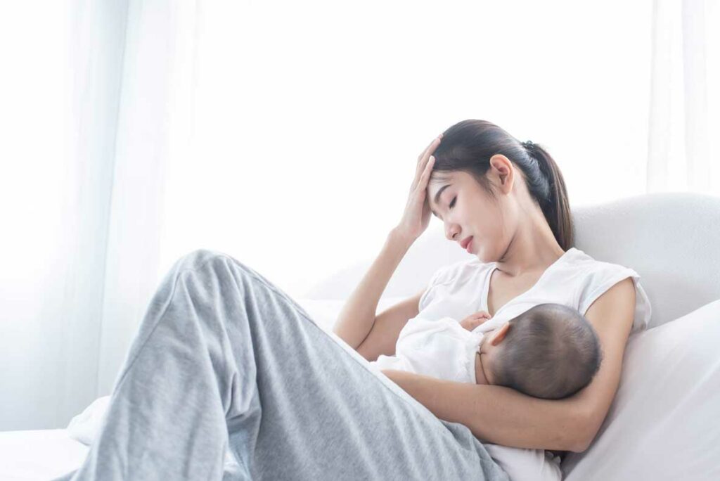 Tired mom breastfeeding baby in bed