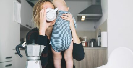 Tired mother drinking coffee while she holds her baby