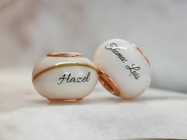 two breastmilk jewelry beads with yellow gold, lock of hair and child's name from KeepsakeMom