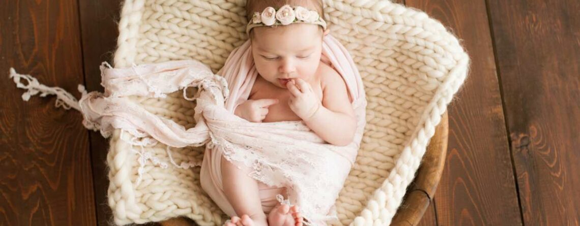 Newborn girl on a brown background in a cozy blanket in a basket