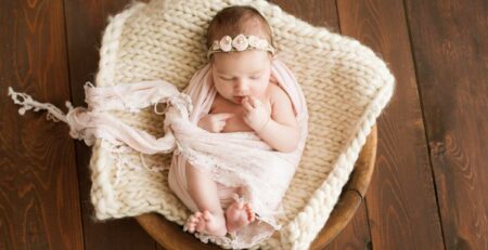Newborn girl on a brown background in a cozy blanket in a basket