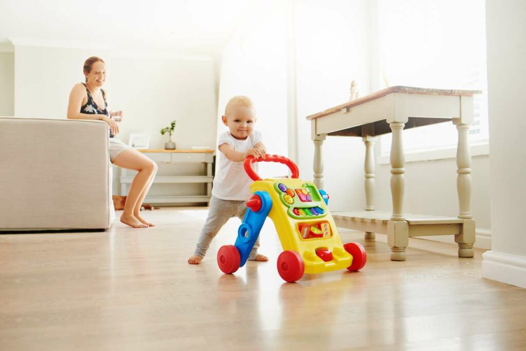 Photo of an baby girl playing with a toy walker at home with mom in the background