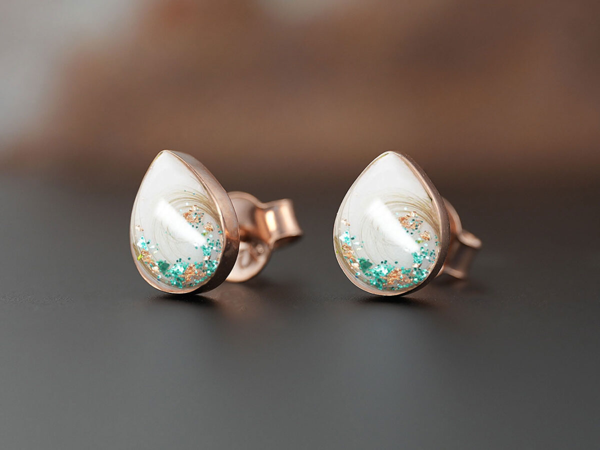 breastmilk pear teardrop shaped studded earrings from KeepsakeMom sterling silver on brown background with green flakes and locks of hair