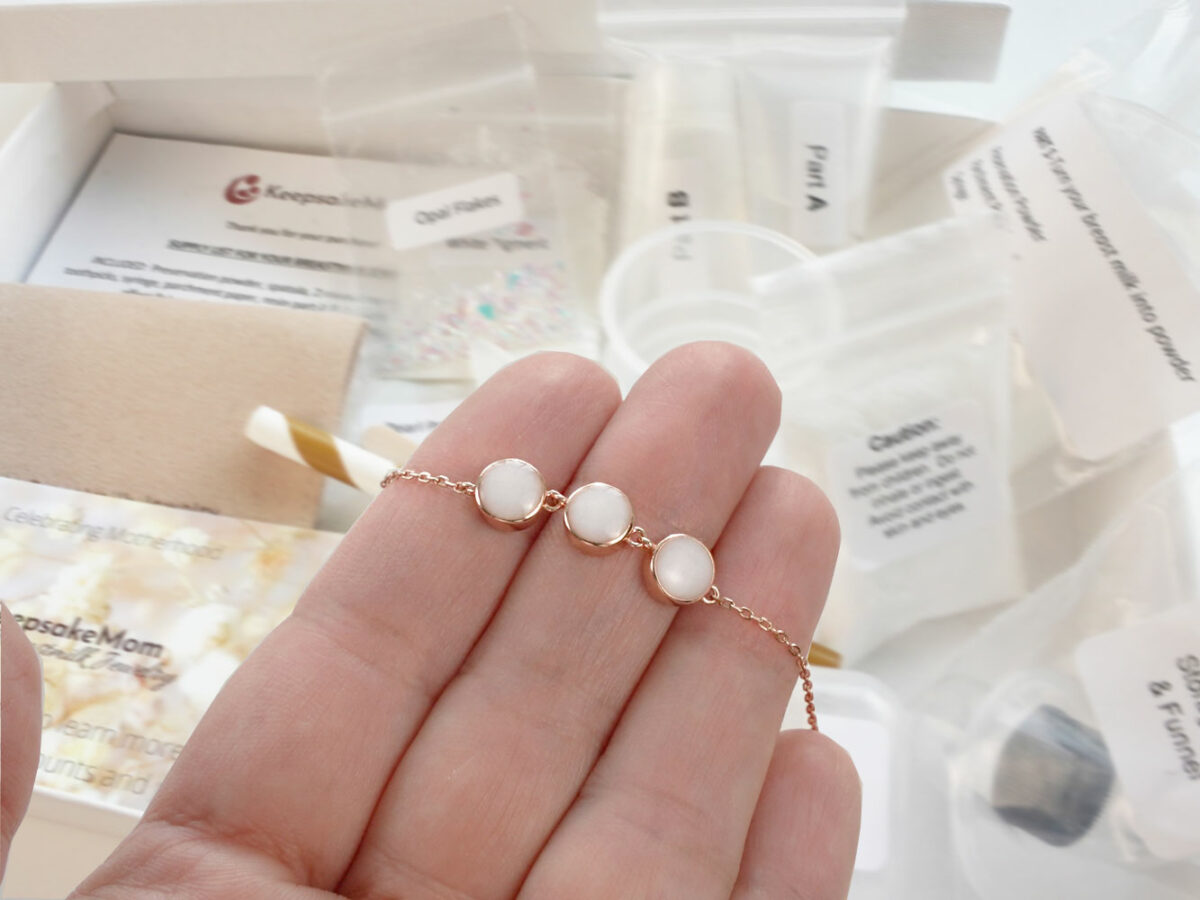 DIY kit breastmilk jewelry three small disc necklace or bracelet shown on a hand for DIY kit from KeepsakeMom on open kit box background