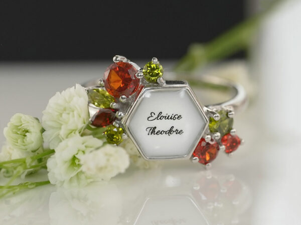 breastmilk ring in hexagon shape milk and honey with different birth month color crystals on each side and name on the milk stone from keepsakemom flowers on the background