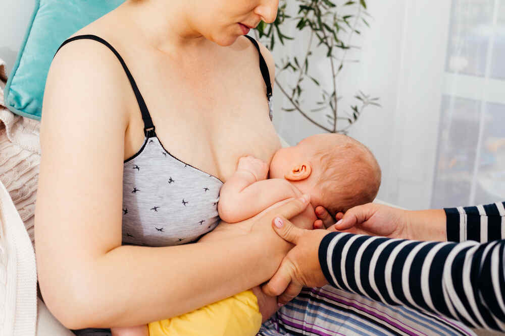 A new mother receives help from a lactation consultant while learning to breastfeed her infant 