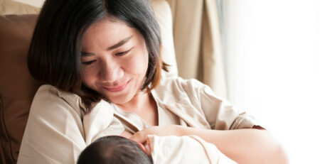 Mother breastfeeding her newborn baby beside window in cross cradle position.