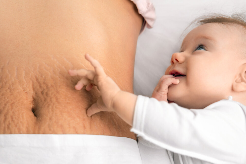 Baby next to mom on bed with postpartum stomach