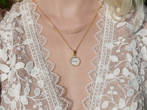 breastmilk jewelry model in white dress wearing round disc to the moon and back necklace with name and lock of hair from KeepsakeMom