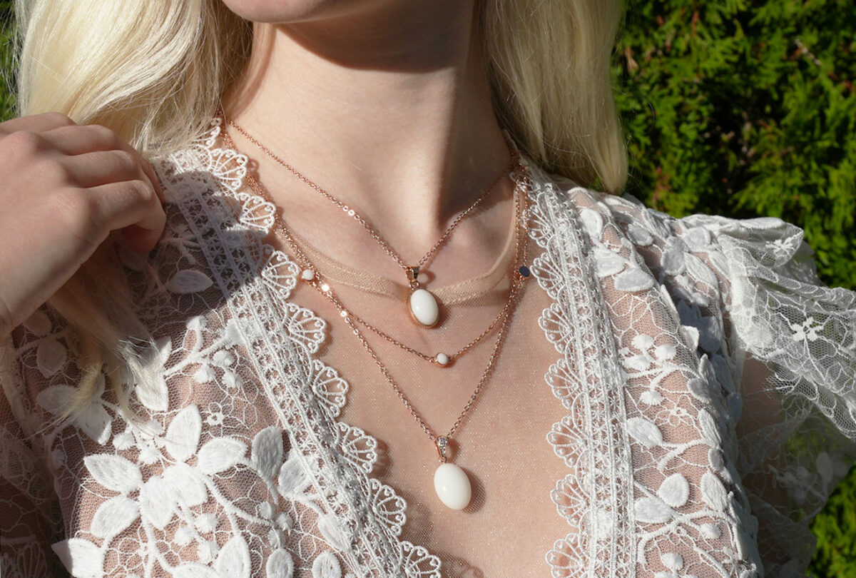breastmilk jewelry model in white dress wearing layered breastmilk necklaces from KeepsakeMom