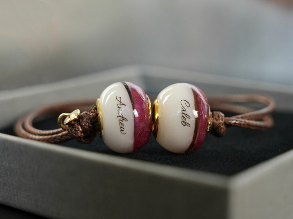 breastmilk jewelry garnet red January birth month color two beads on the bracelet half with breastmilk with children's lock of hair and names on the waxed brown cord from KeepsakeMom