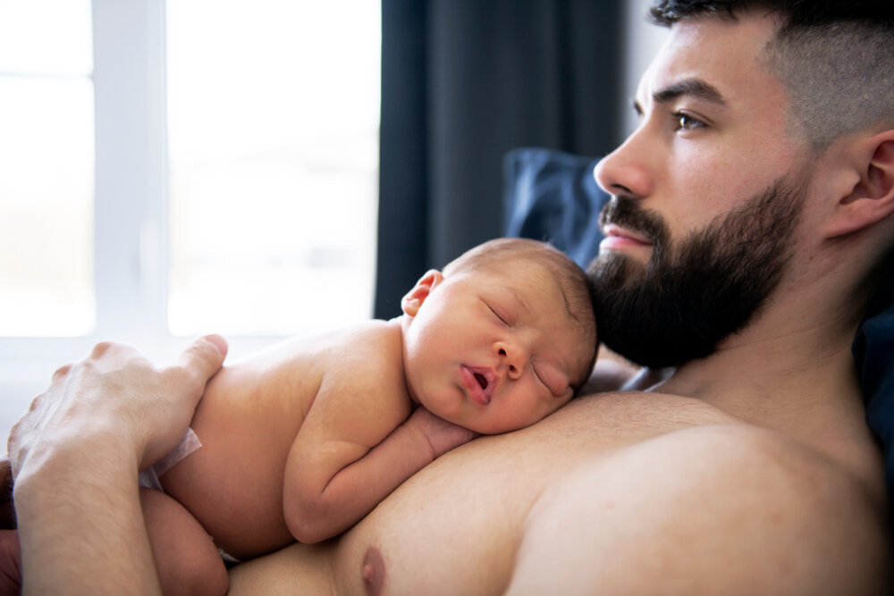 Dad practicing kangaroo care with newborn in bed 