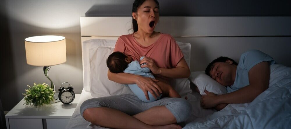 Tired mom cluster feeding newborn at night in bed