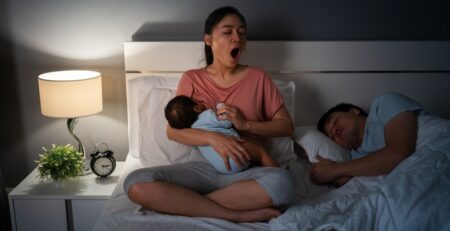 Tired mom cluster feeding newborn at night in bed