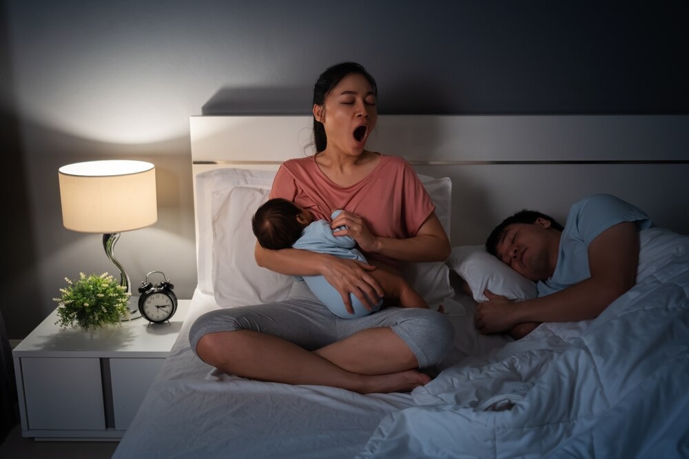 Tired mom cluster feeding newborn at night in bed