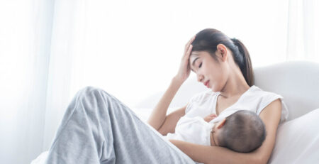Stressed mom on bed breastfeeding newborn
