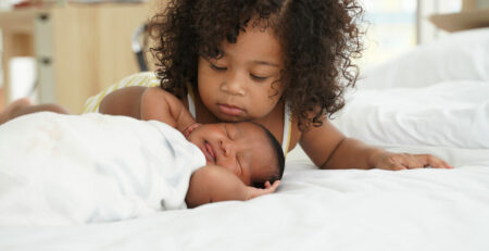 Older sibling cuddling baby sibling on bed