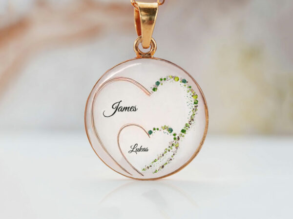 breastmilk jewelry large disc filled with breastmilk and two hearts one within another with green shimmers of one side of the hearts made with hair from keepsakemom