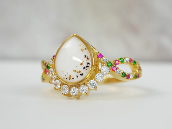 breast milk ring with birth month crystals around teardrop shaped milk stone and yellow gold plating and placenta flakes in the stone from keepsakemom