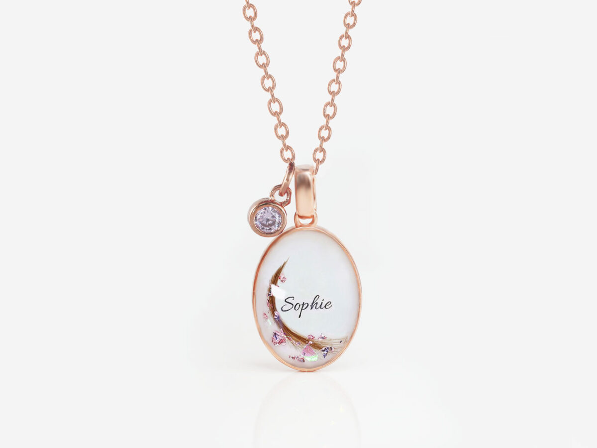 breastmilk jewelry oval simple necklace from keepsakemom in rose gold setting on white background with flakes, hair, name and tiny purple charm