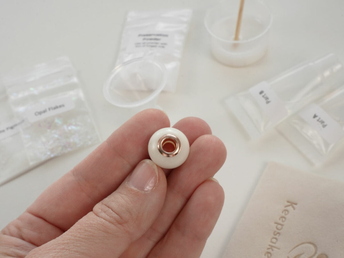 DIY kit breastmilk jewelry bead shown on a hand for DIY kit from KeepsakeMom on open kit box background