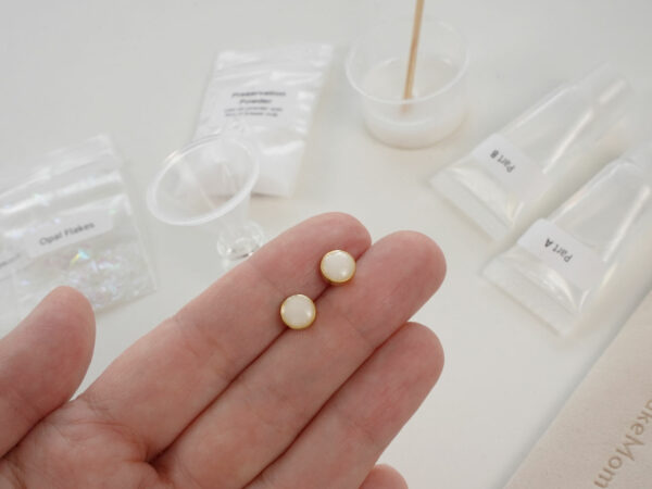 DIY kit breastmilk jewelry round disc earrings shown on a hand for DIY kit from KeepsakeMom on open kit box background