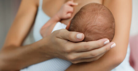 Mother cradling head of newborn baby breastfeeding