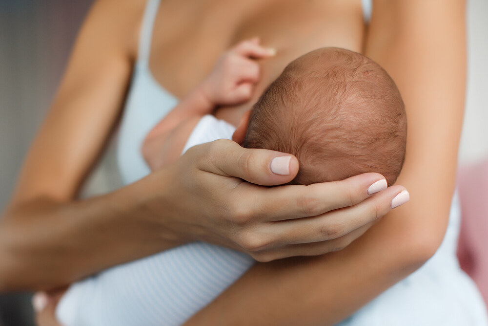 Mother cradling head of newborn baby breastfeeding