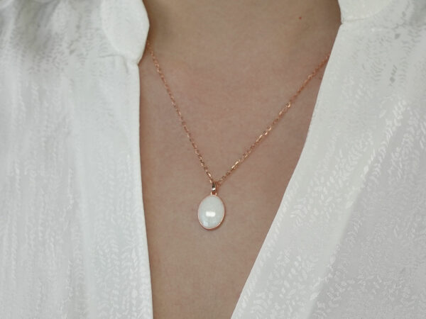 breastmilk jewelry oval simple necklace from keepsakemom in rose gold setting on light background with pearl powder in milk stone on model chest