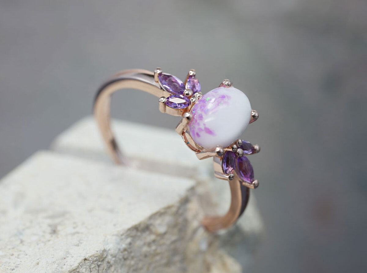 breastmilk ring burst of love oval with purple february three crystals on each side of the breastmilk oval stone with alexandrite crushed gems from KeepsakeMom in rose gold placed on a stone side view