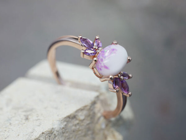 breastmilk ring burst of love oval with purple february three crystals on each side of the breastmilk oval stone with alexandrite crushed gems from KeepsakeMom in rose gold placed on a stone side view